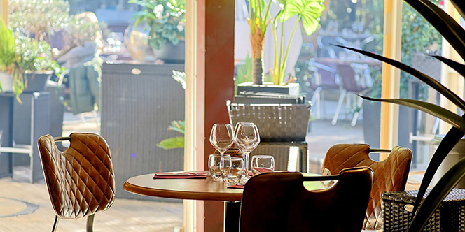 L'Effet Jardin Lattes : table dressée avec verres à vin et fauteuils en cuir, près des baies vitrées donnant sur le patio végétalisé.